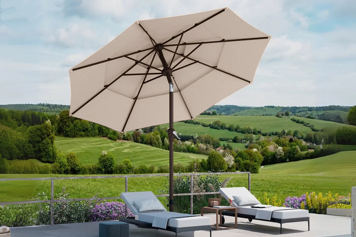 Beige patio umbrella with lounge chairs on a terrace overlooking green fields and hills.