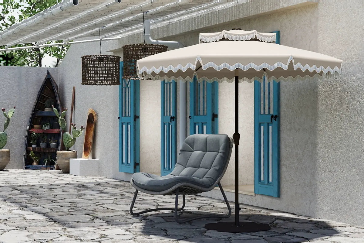 Beige patio umbrella with decorative trim over a gray chair on a stone patio.