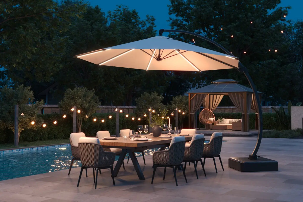 Outdoor dining setup with a large illuminated umbrella over a table by a pool at night.