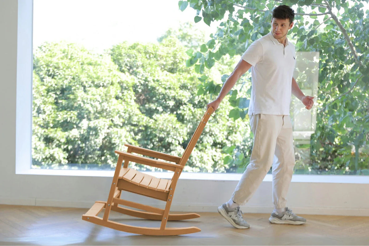 Person pushing a wooden rocking chair indoors with a large window in the background