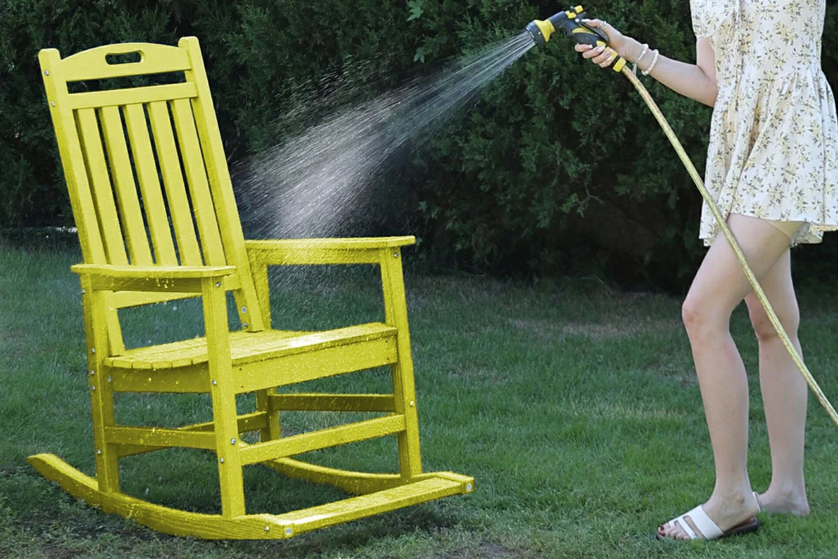 Person cleaning a yellow rocking chair with a hose on a grassy area.