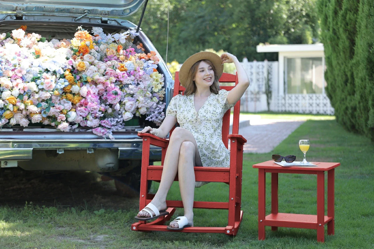 Woman sitting on a red chair next to a truck filled with flowers, with a table and sunglasses nearby.