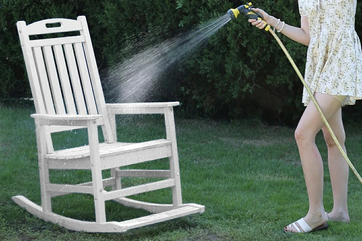 Person cleaning a white rocking chair with a hose on a grassy area.