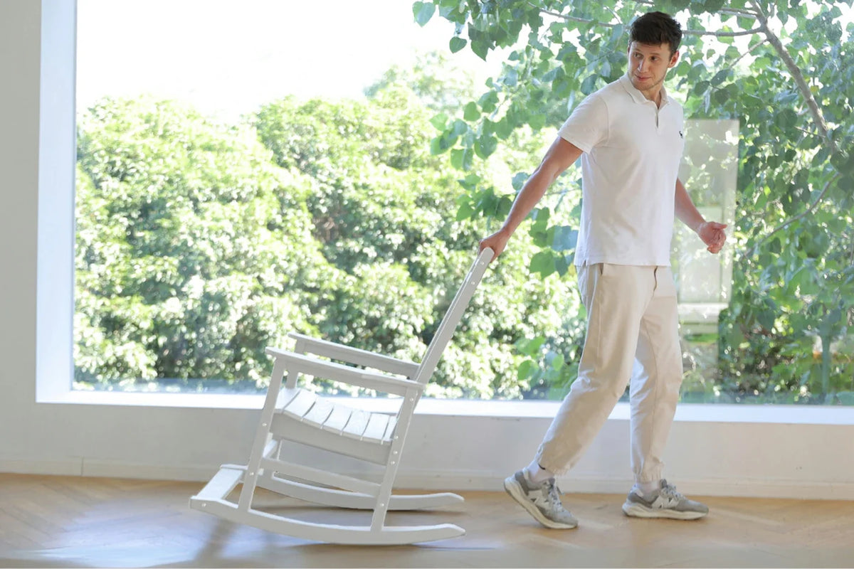 Person moving a white rocking chair indoors with greenery outside