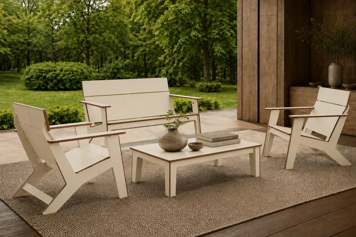A beige 4-piece outdoor patio conversation set including a loveseat, two armchairs, and a coffee table arranged on a woven rug in a garden setting.
