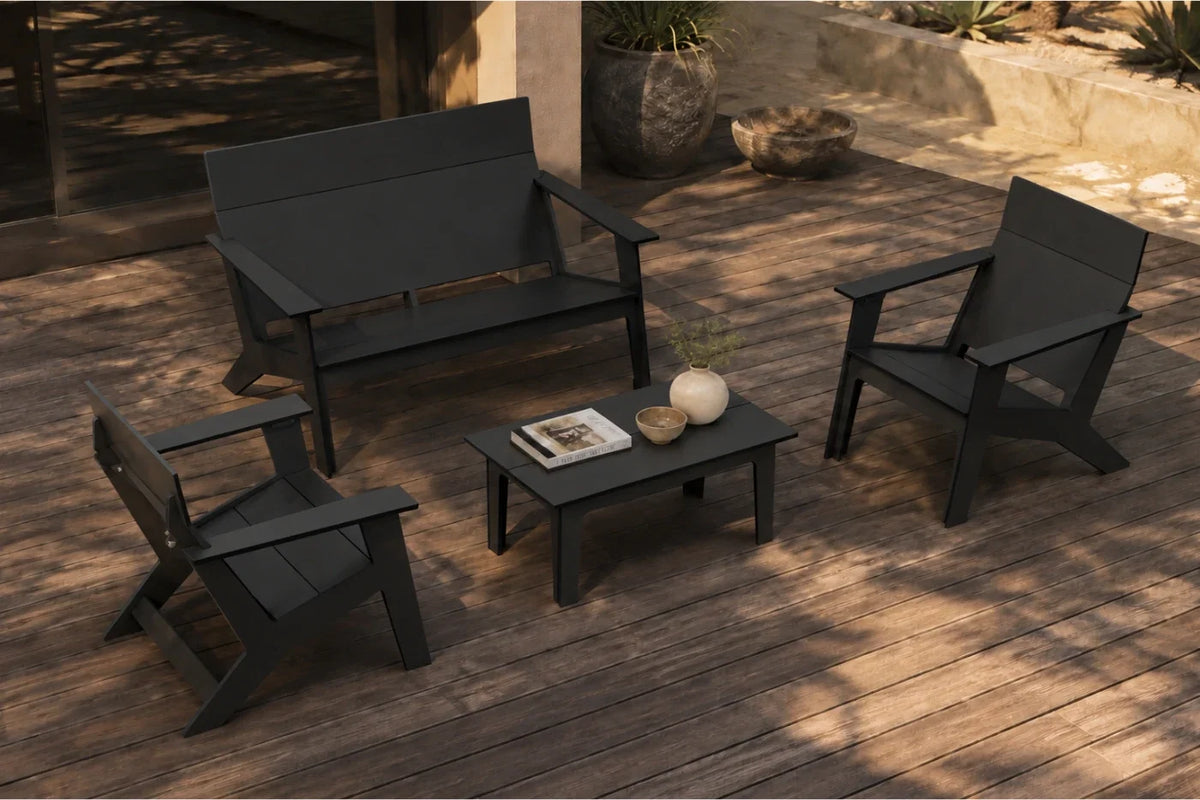 A four-piece outdoor patio furniture set in black, including a loveseat, two armchairs, and a small rectangular coffee table, arranged on a wooden deck with decorative props.