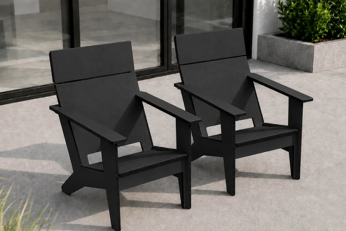 Two modern black outdoor Adirondack-style chairs placed on a light concrete patio in front of large glass doors, with a planter visible in the background.