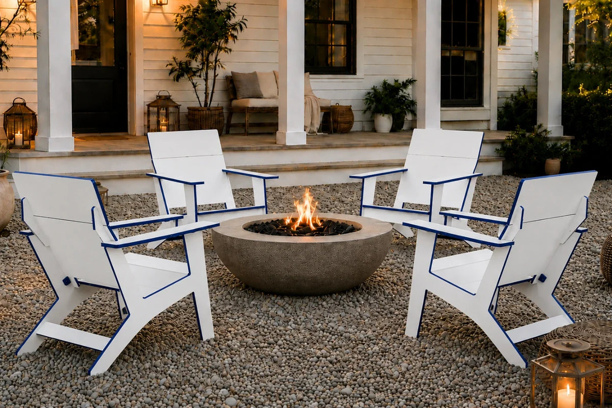 Four white outdoor Adirondack-style chairs with blue trim arranged around a round concrete fire pit on a gravel patio in front of a house porch.