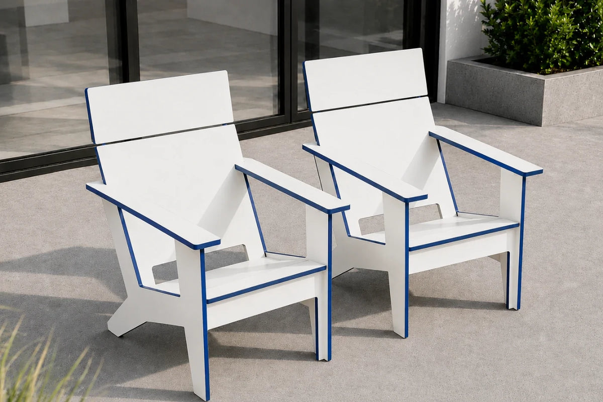 Two modern outdoor Adirondack-style chairs in white with blue trim, shown on a concrete patio in front of a glass door.