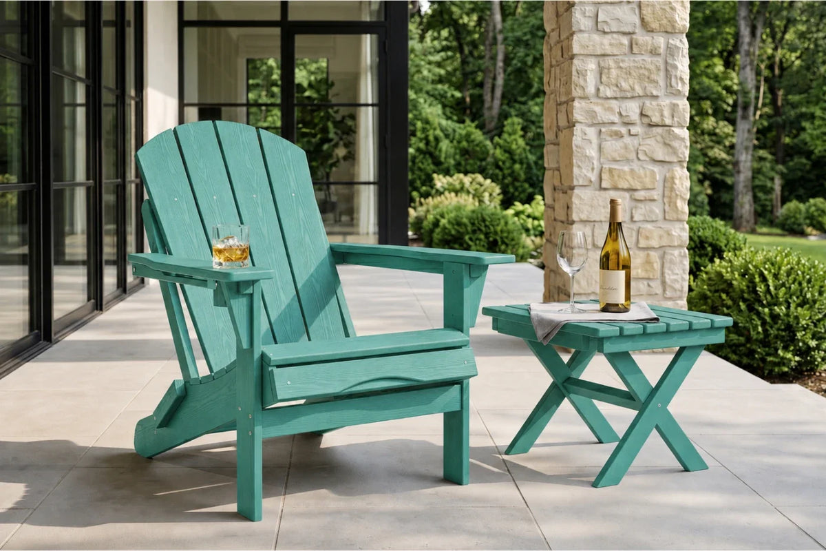 An aruba blue outdoor Adirondack chair sits on a patio beside a matching small side table with a wine bottle and glass, with a stone column and green garden in the background.
