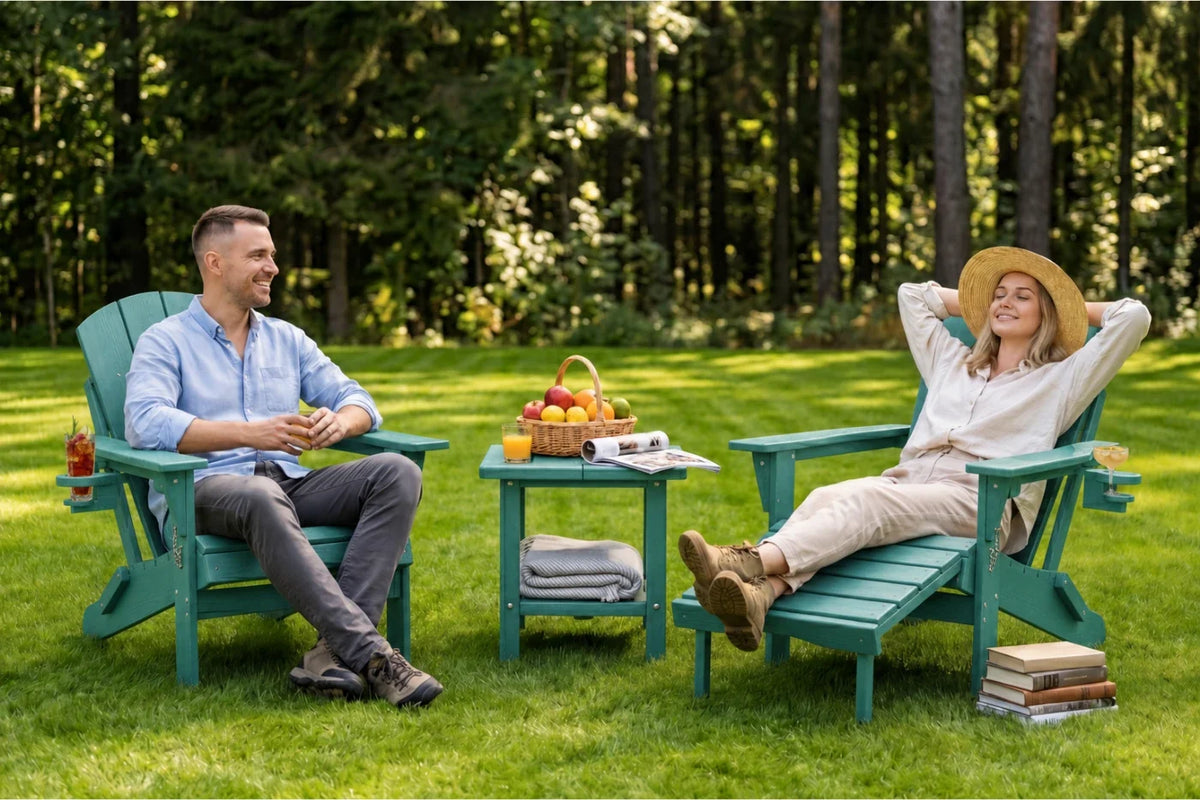 A man and a woman relax in matching aruba blue Adirondack chairs on a grassy lawn with a small table between them, set against a backdrop of a dense green forest.