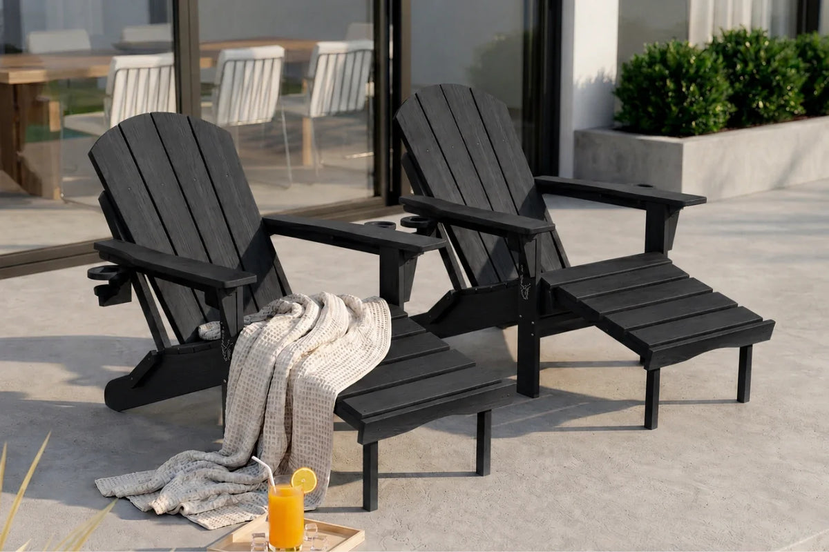Two black outdoor Adirondack-style chairs with matching footrests on a patio, with a draped throw blanket and a glass of orange juice in the foreground.