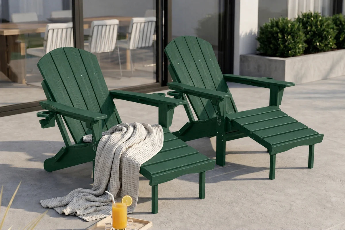Two dark green outdoor Adirondack chairs with matching footrests on a concrete patio, with a gray throw blanket and a glass of orange juice in the foreground.