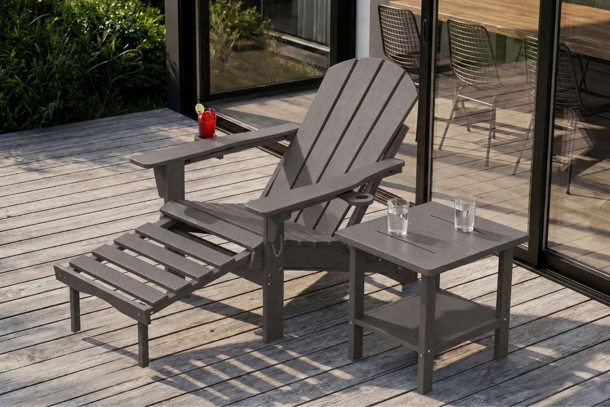 A dark gray HDPE reclining adirondack chair with a matching footrest and a small side table, placed on a wooden deck next to glass doors.