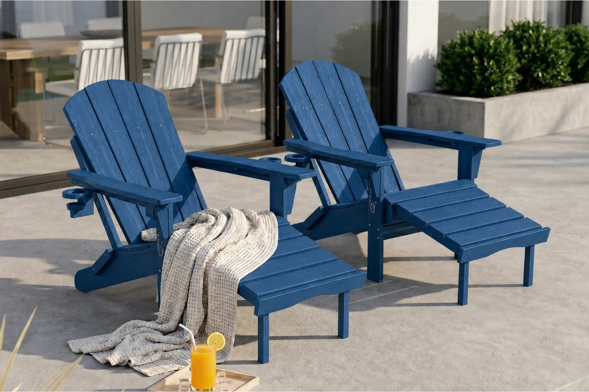 Two navy blue outdoor Adirondack chairs with matching footrests on a patio, styled with a draped throw blanket and a glass of orange juice.