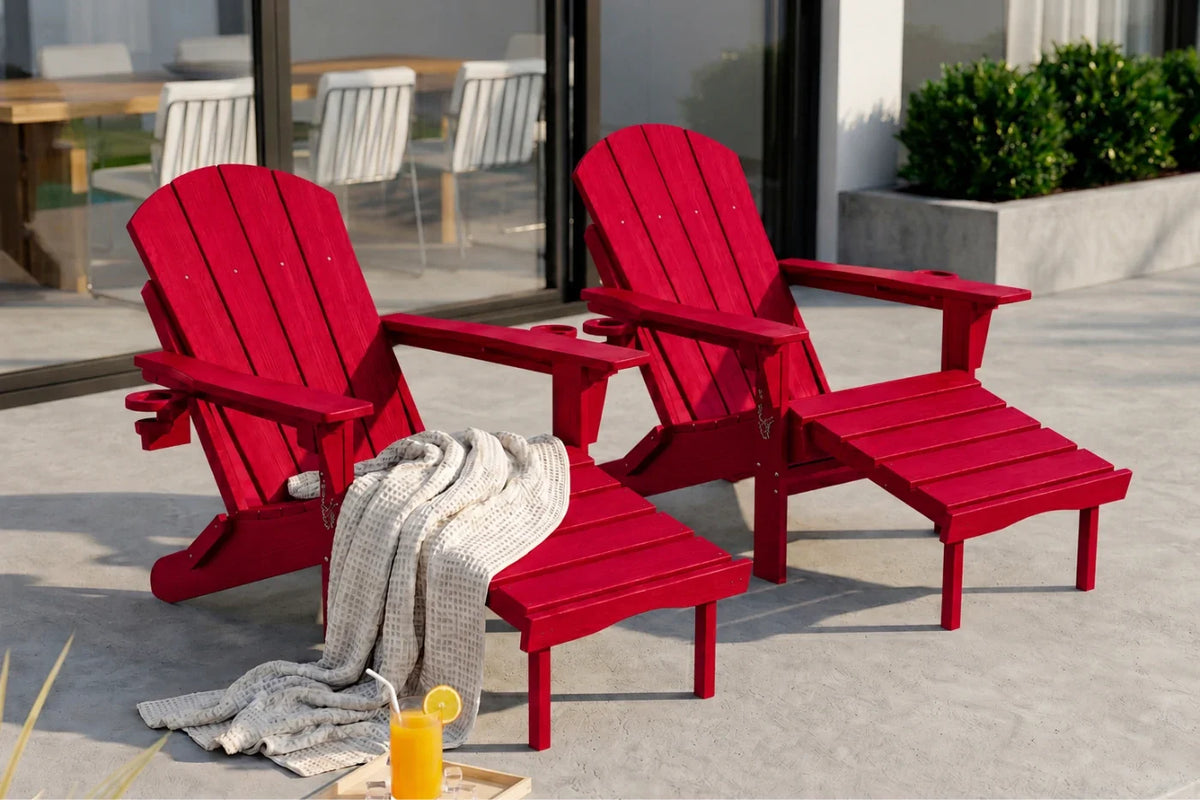 Two red outdoor Adirondack chairs with matching footrests on a light concrete patio. A light gray knit throw blanket is draped over the seat of the front chair, and a small tray with an orange drink sits nearby.