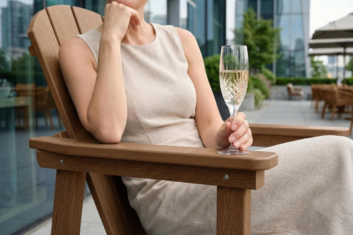 Woman sitting in a brown chair outdoors, holding a glass of champagne.