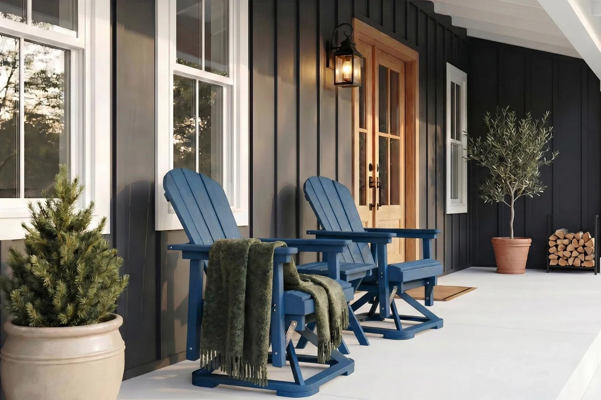 Two navy blue Adirondack chairs on a porch with a black house and potted plants.