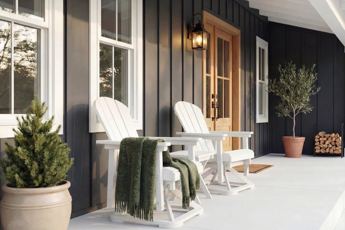 Two white Adirondack chairs on a porch with a green blanket, potted plants, and a wooden door.