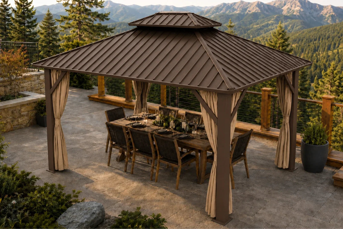 A large hardtop gazebo with netting and curtains, sheltering a wooden dining table and chairs on a stone patio with a mountain forest backdrop.
