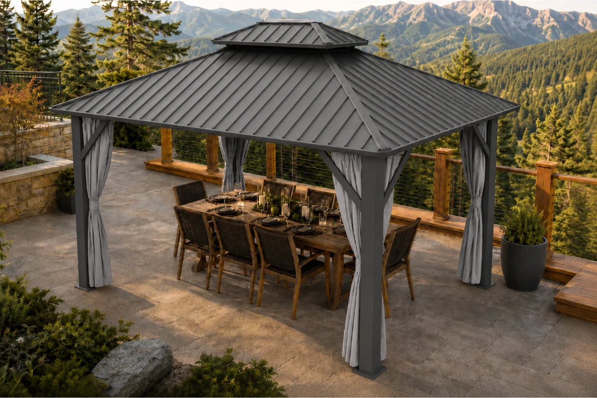 A dark gray hardtop gazebo with netting and curtains, sheltering a wooden dining table and chairs. The gazebo is situated on a stone patio with a scenic mountain and pine forest background.