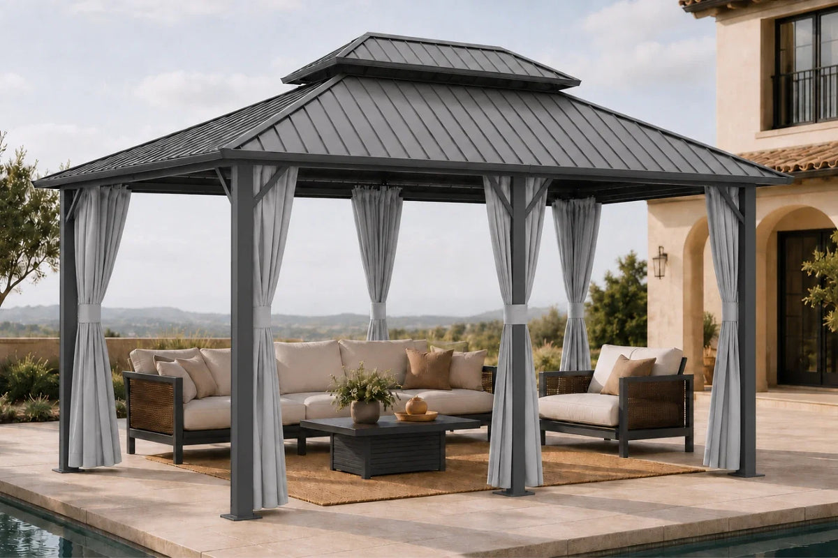 A dark gray hardtop gazebo with netting and curtains, furnished with a beige sectional sofa, coffee table, and rug, situated on a patio next to a swimming pool with a house in the background.