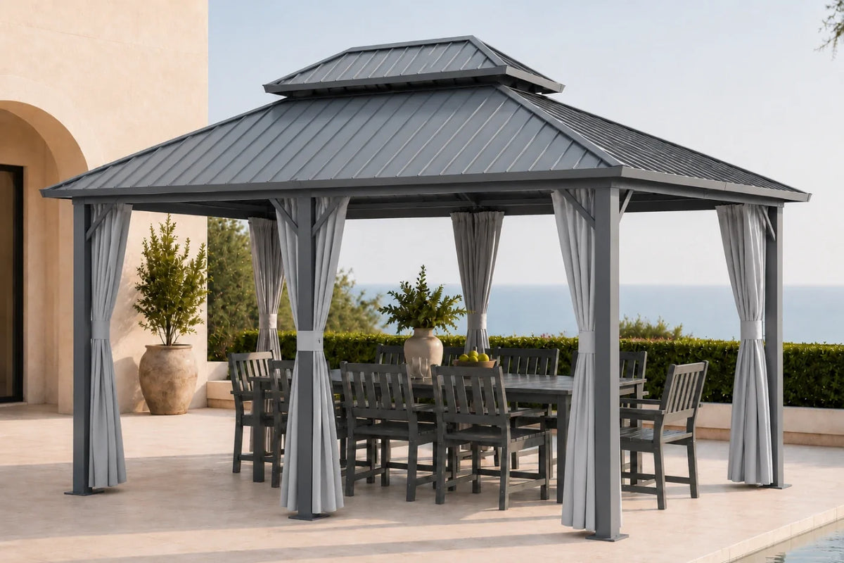 A dark gray hardtop gazebo with netting and curtains, housing a matching dark gray dining table and chairs. The gazebo is situated on a tiled patio with a beach and ocean view in the background.
