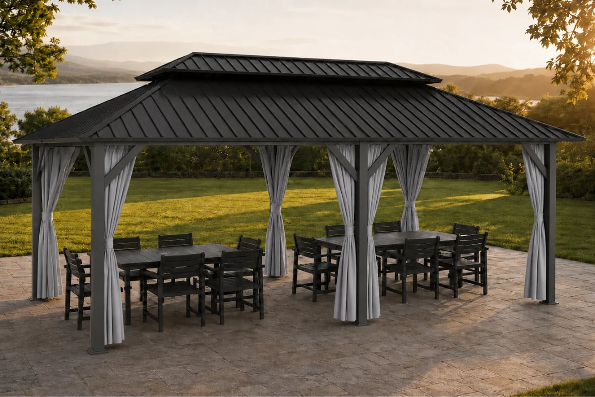 A dark gray hardtop gazebo with netting and curtains, sheltering a dining set on a stone patio with a grassy lawn and distant water landscape in the background.