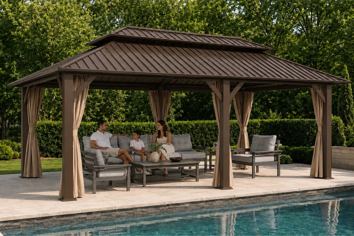 A large outdoor double-roof gazebo with curtains and a brown roof, situated next to a swimming pool. Underneath, a man and a woman are seated on a gray outdoor sofa with a coffee table, with two matching armchairs on the right.