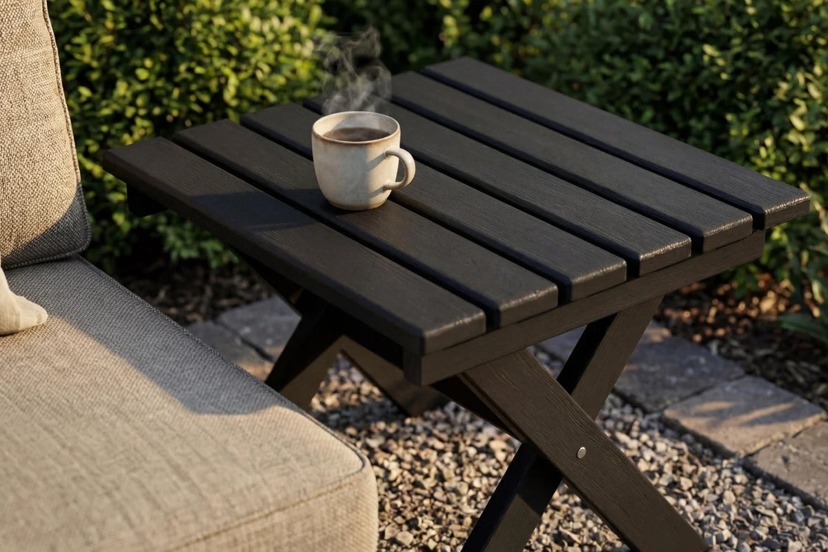 Black outdoor table with a steaming cup on it, next to a beige chair.