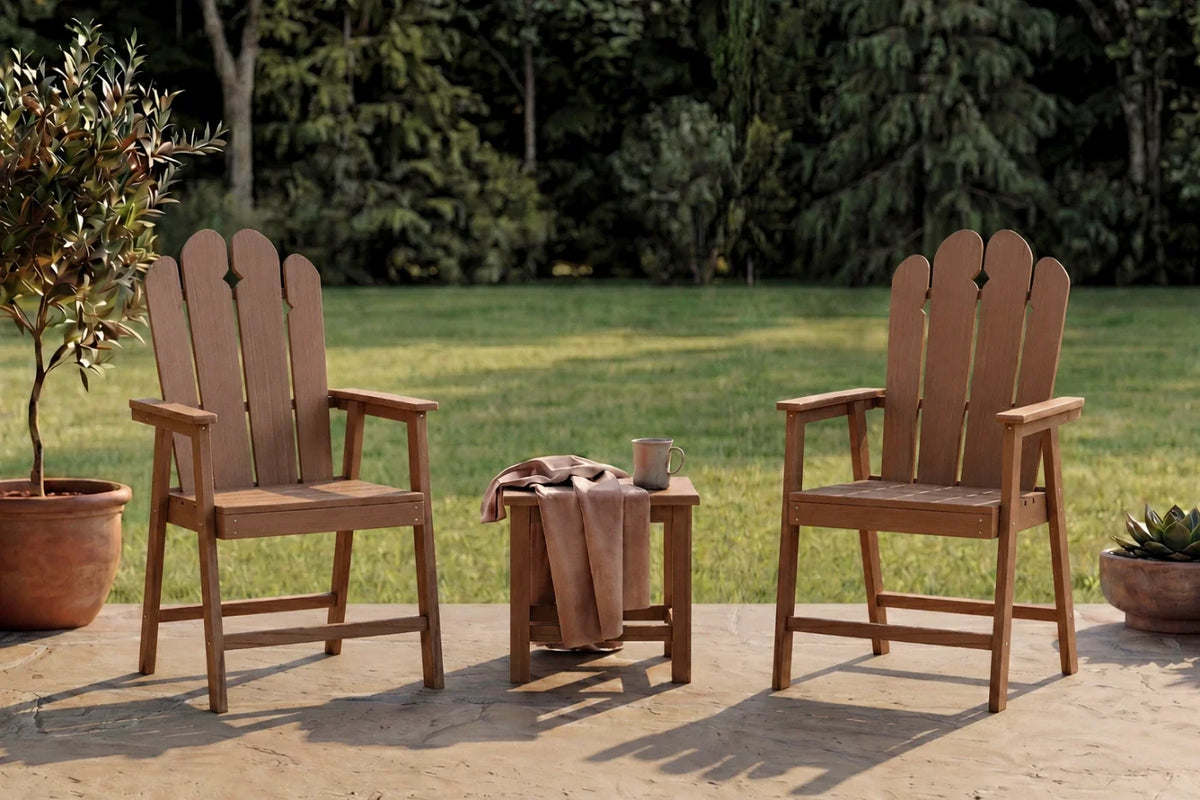 Two light brown Adirondack chairs with a small table on a patio with greenery in the background.