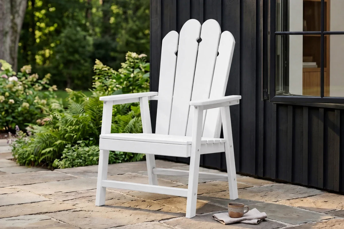 White HDPE chair on a stone patio with greenery and a building in the background