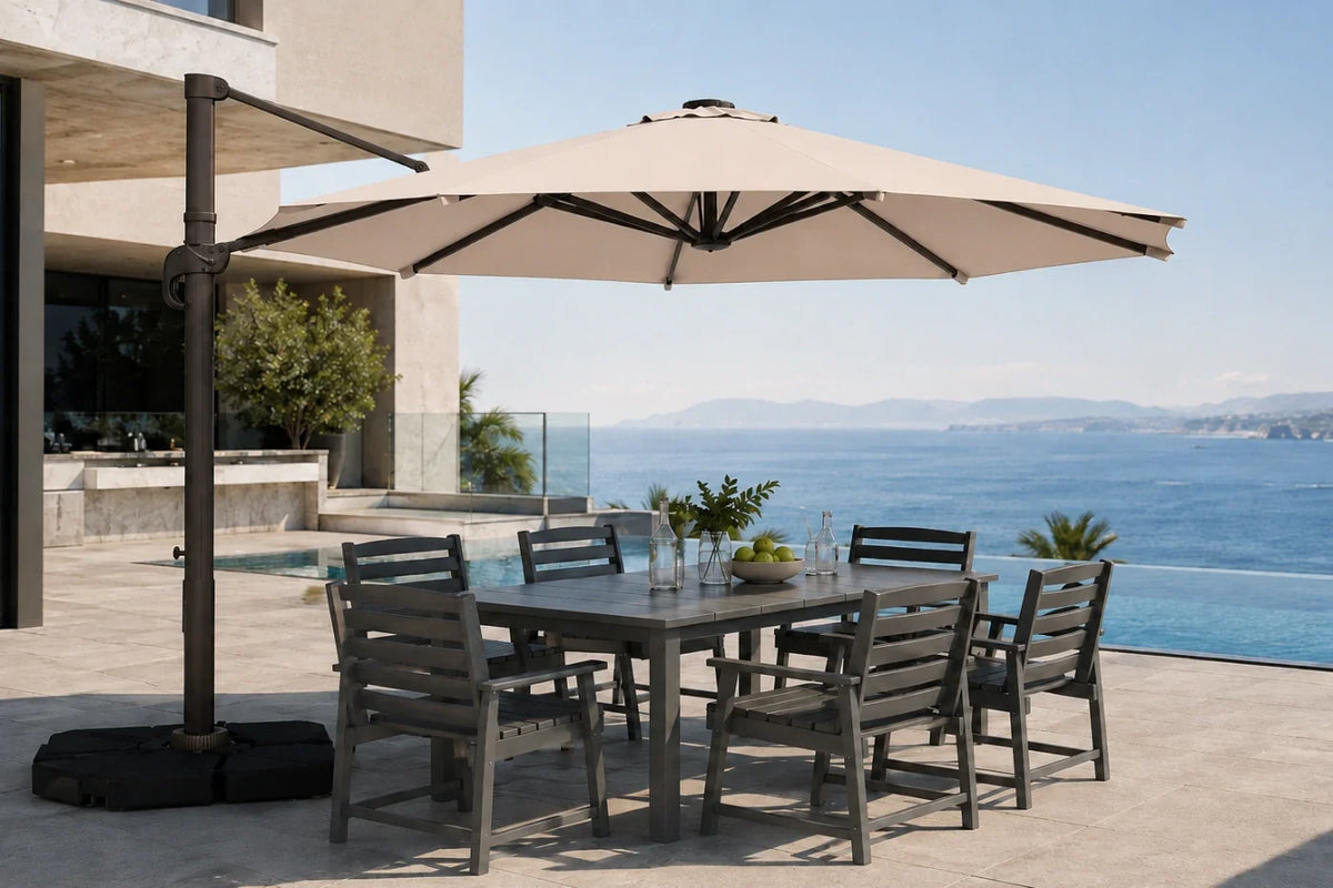 Outdoor patio dining set with a rectangular gray table and six matching slatted chairs under a large beige cantilever umbrella, overlooking a pool and ocean view.
