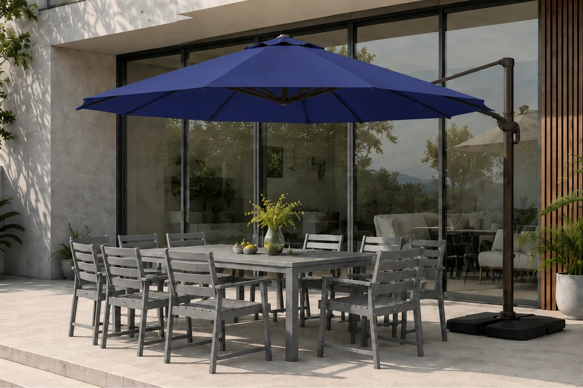 A large navy blue cantilever patio umbrella with a black metal frame and base, shading a gray outdoor dining table and chairs on a stone patio in front of a modern glass building.