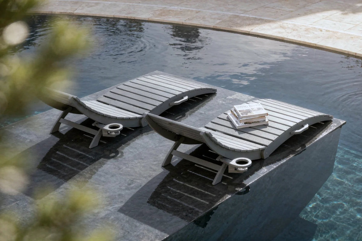 Two lounge chairs by a pool with a book on one of them.