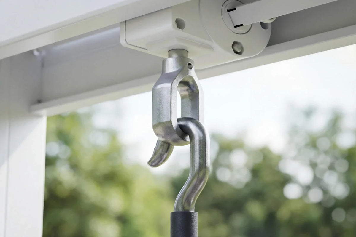 Metal bracket attached to a window frame with a blurred green outdoor background