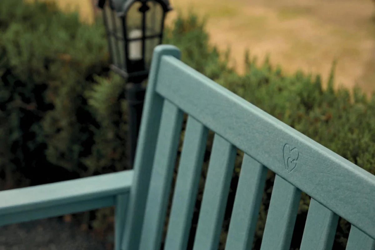 Teal bench with a blurred background of greenery and a lamp post.