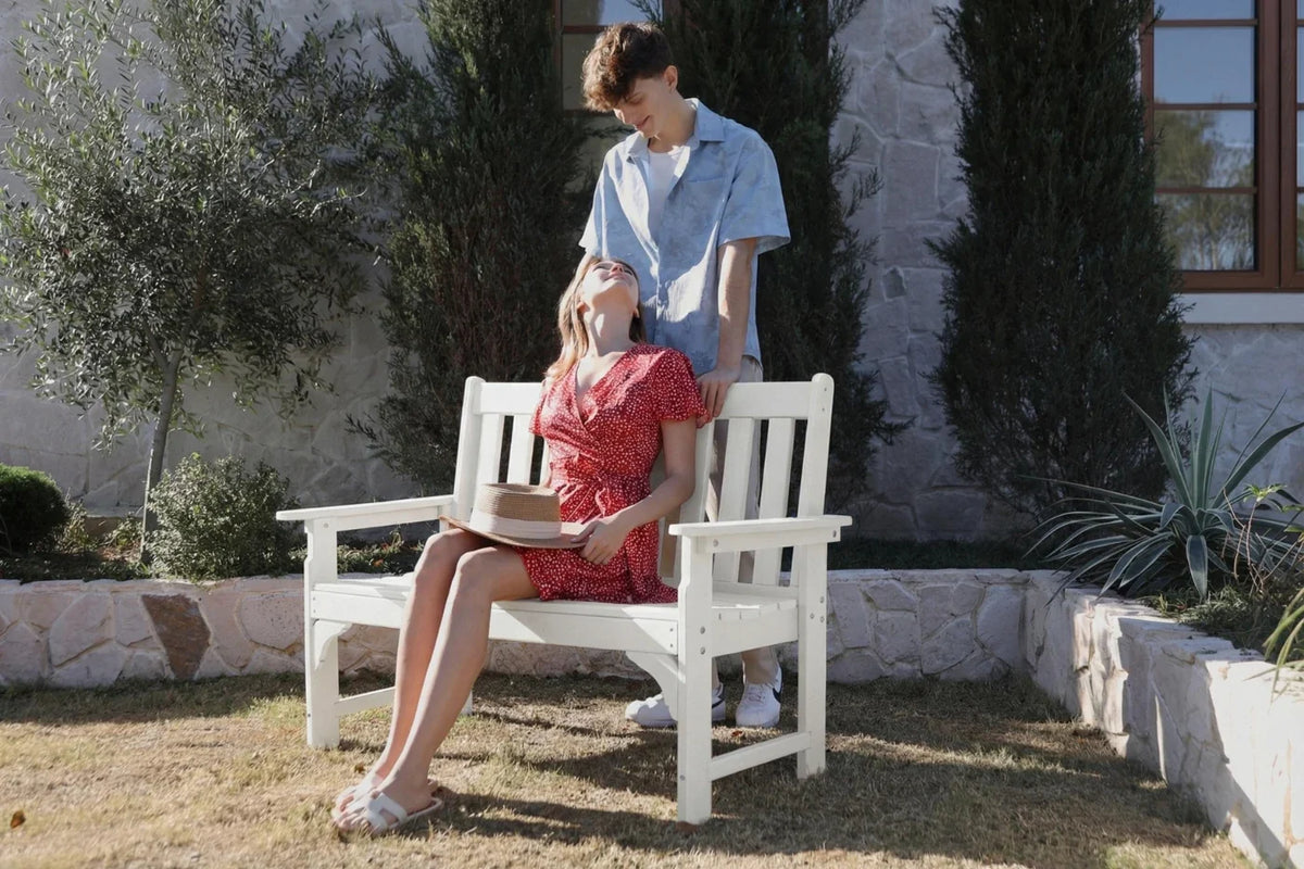 Two people sitting on a white bench in a garden setting.