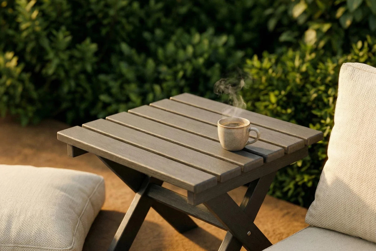 Small wooden table with a cup on it, surrounded by outdoor furniture and greenery.