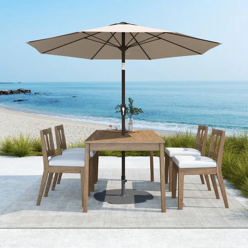 Outdoor dining set with table and chairs under a large umbrella by the beach.