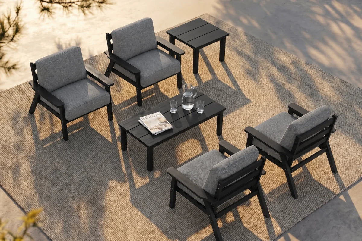 A 6-piece outdoor patio conversation set including four gray cushioned armchairs, one matching rectangular coffee table and one matching side table, arranged on a textured beige rug over concrete pavers.