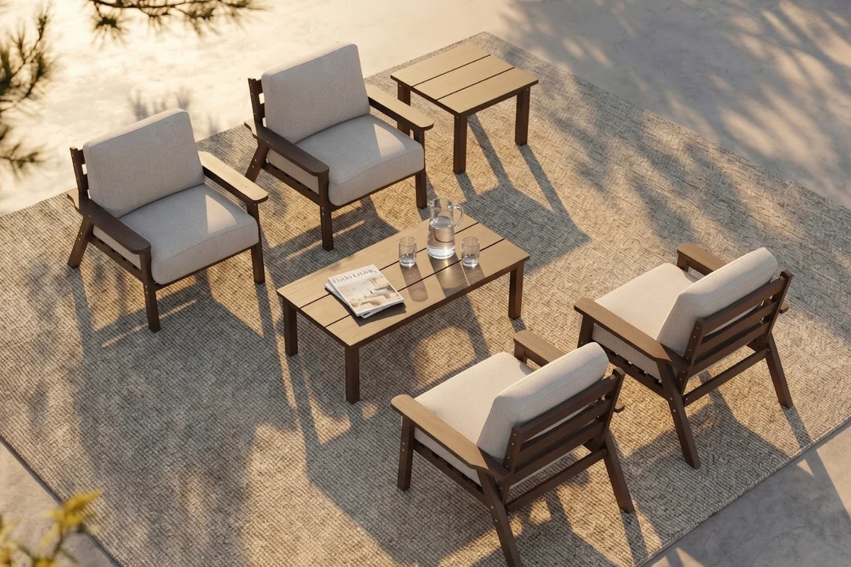 A 6-piece outdoor patio conversation set with four armchairs with creamy white cushions, one matching rectangular coffee table, and one matching side table, arranged on a textured beige rug.