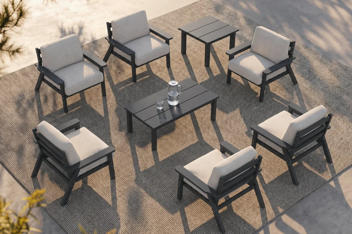 An 8-piece outdoor patio furniture set arranged on a woven rug, featuring six gray armchairs with creamy white cushions, one matching rectangular coffee table, and one matching side table.