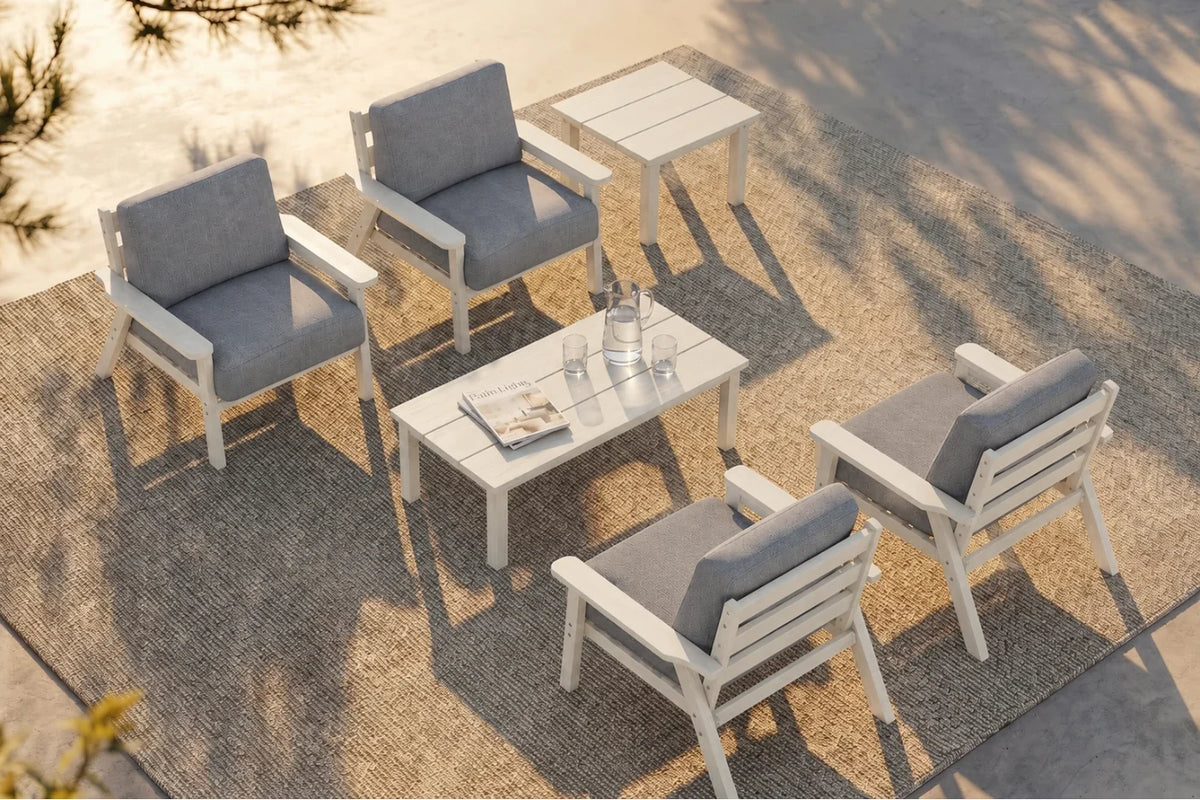 A 6-piece outdoor patio conversation set including four white armchairs with gray cushions, one matching rectangular coffee table, and one matching side table, arranged on a textured beige rug.