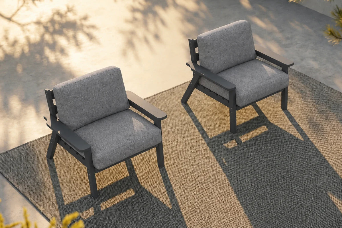Two modern outdoor armchairs with gray textured cushions and dark gray frames, positioned on a concrete patio with long shadows under warm sunlight.