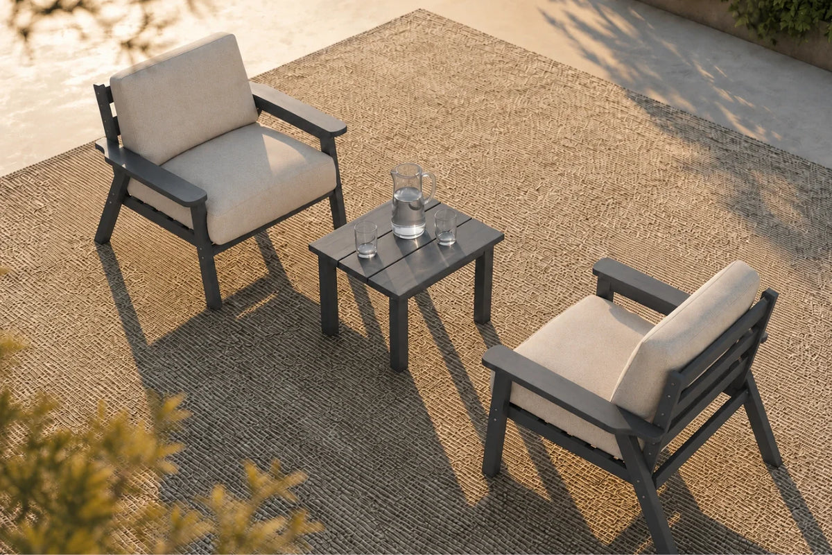 Two outdoor armchairs with creamy white cushions and dark gray frames, arranged around a matching square side table on a textured patio rug.