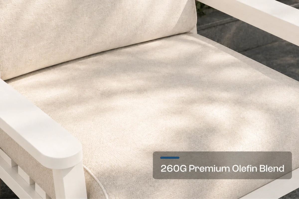 Close-up of a creamy white outdoor chair cushion with a white frame, showing dappled sunlight and a text overlay that reads '260G Premium Olefin Blend'.
