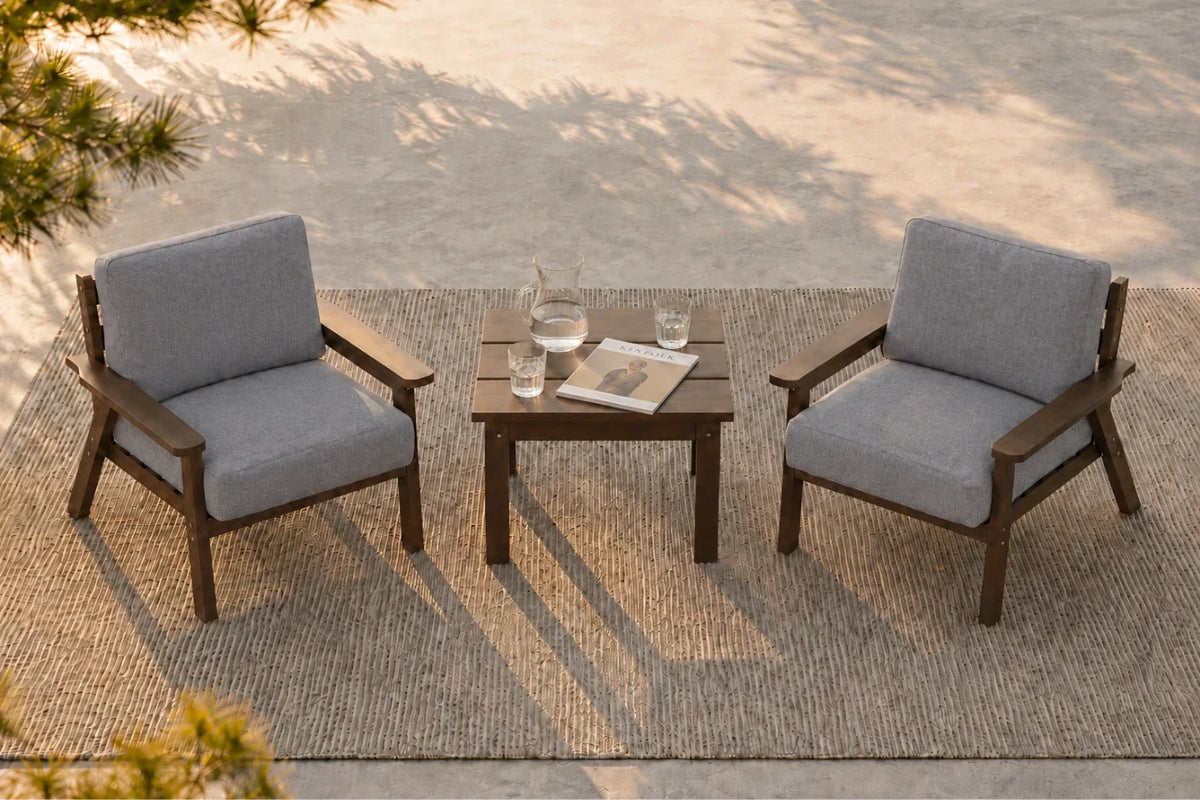Two gray outdoor armchairs with brown frames are arranged on a woven rug around a small square side table in a patio setting.