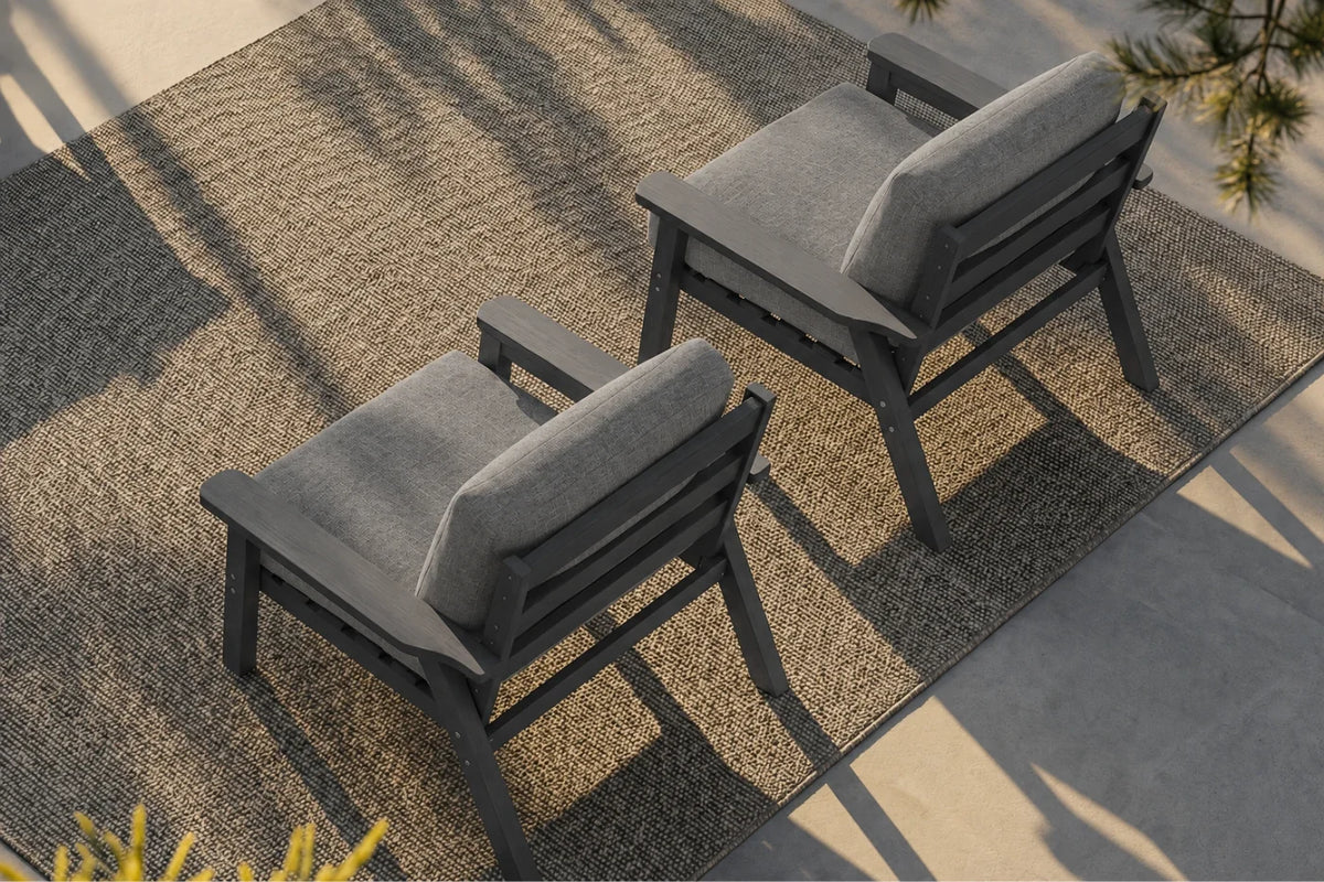 Two outdoor armchairs with dark gray frames and gray cushions, arranged on a textured beige rug over a concrete patio.