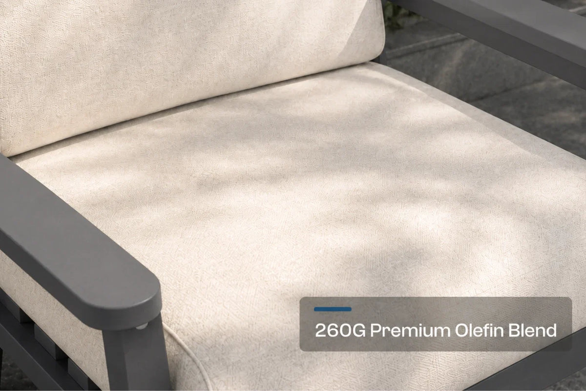 Close-up of a patio chair cushion in a creamy white fabric with a dark gray frame, featuring a text overlay that reads '260G Premium Olefin Blend'.